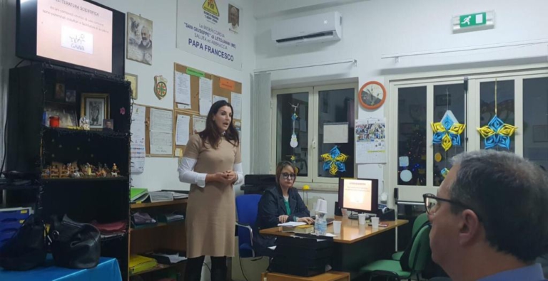 Relatrice in piedi accanto a un tavolo con il pubblico in primo piano