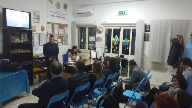 Pubblico seduto in sala e relatore in piedi durante la presentazione del libro