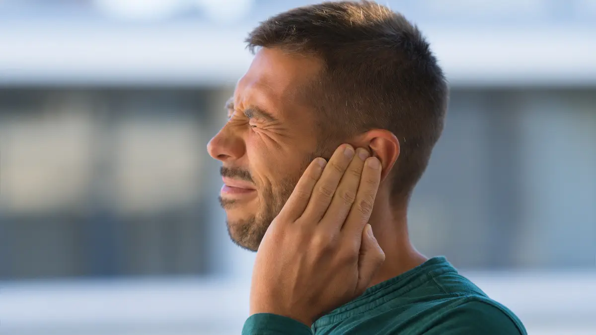 Uomo con la mano sull’orecchio e un’espressione di fastidio